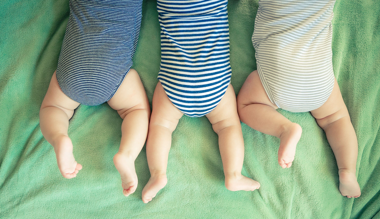 Drei Babys auf dem Bauch liegend.