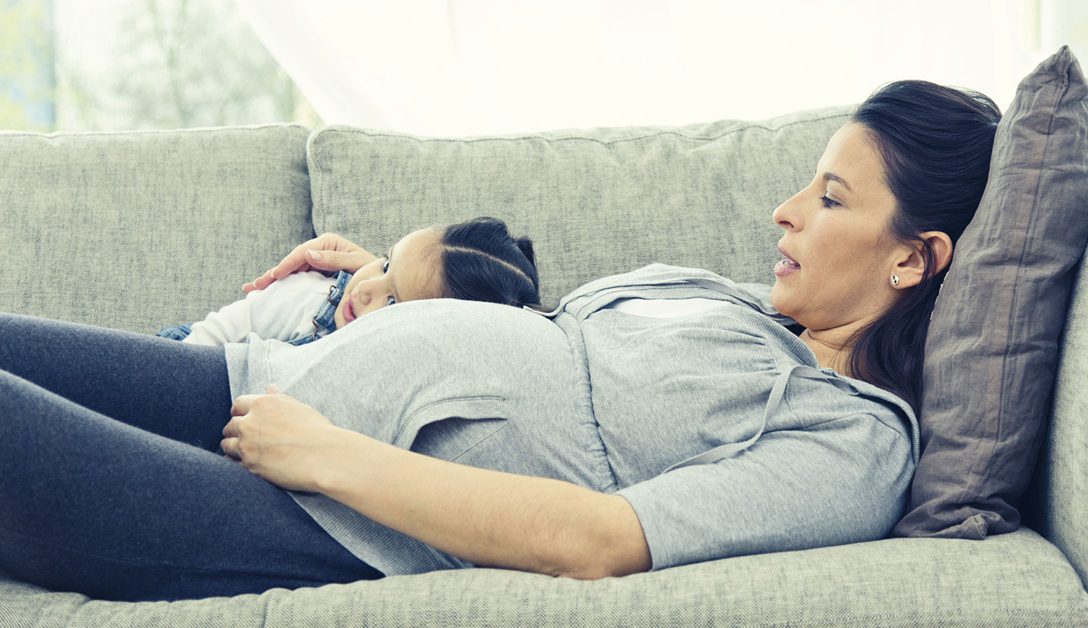 Schwangere Mutter liegt mit Tochter auf dem Sofa
