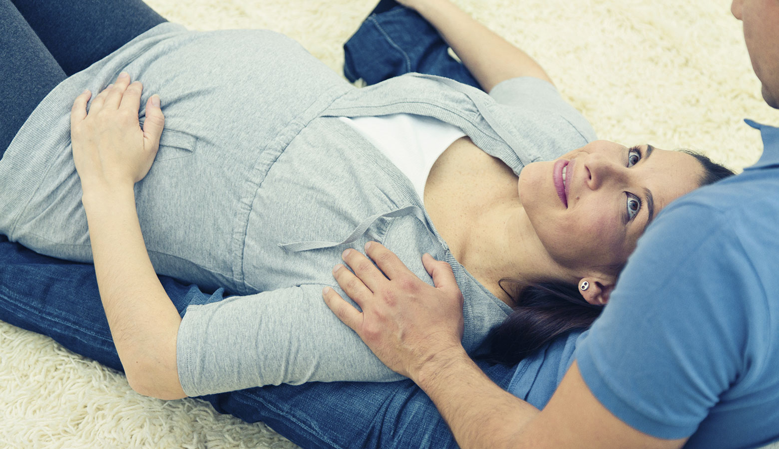 Schwangere liegt am Boden in den Armen des Partners.