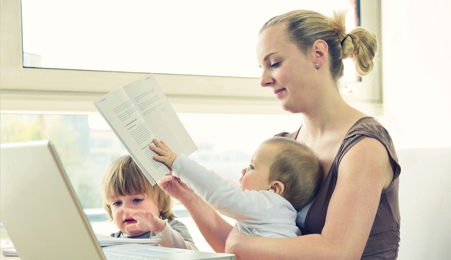 Mutter mit zwei Kleinkindern am Laptop sitzend. 