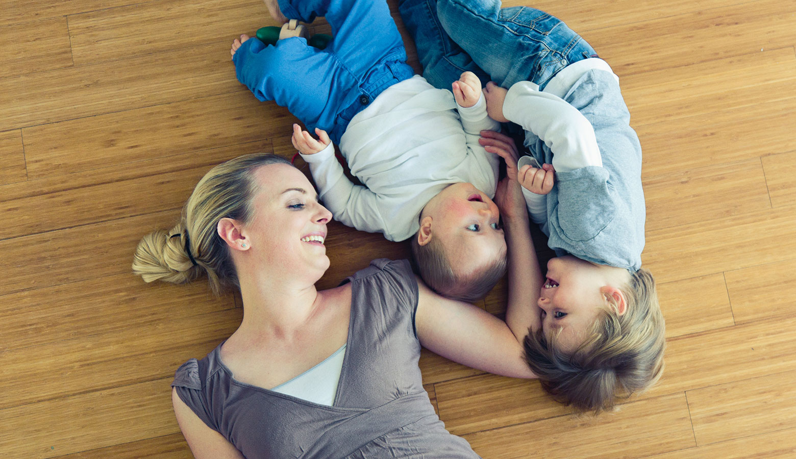 Mutter liegt mit ihren beiden Kleinkindern am Boden. 