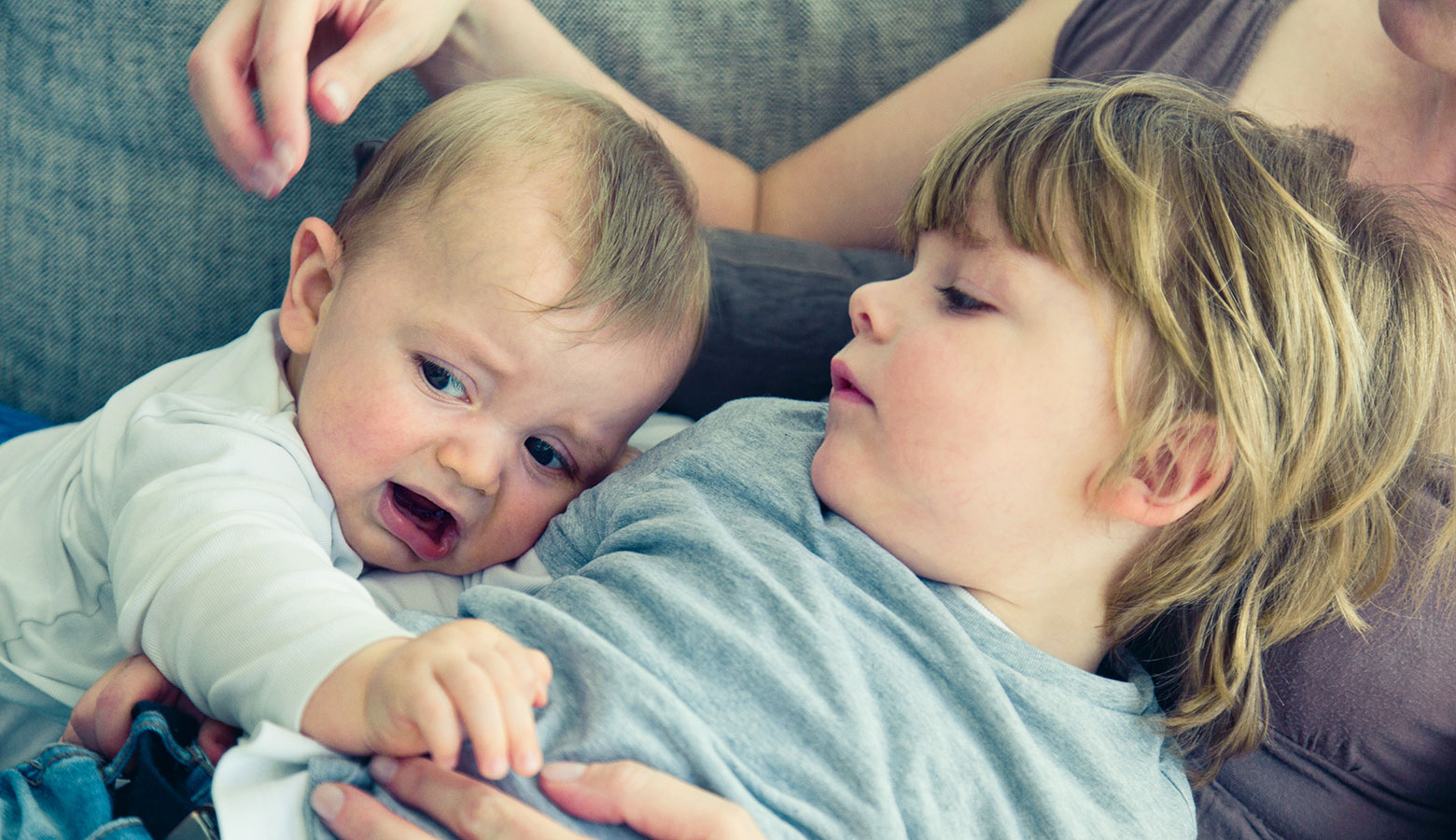 Zwei Kleinkinder liegen bei der Mutter auf der Couch