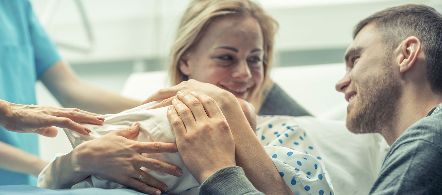 Im Krankenhaus-Zimmer: Mutter und Vater streicheln Neugeborenes. 