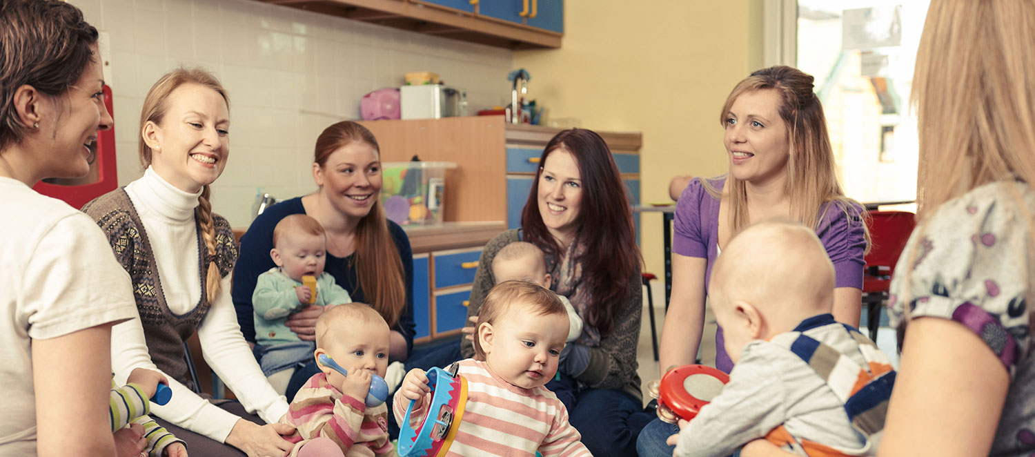 Eine Gruppe von Müttern mit spielenden Babys sitzt im Kreis. 