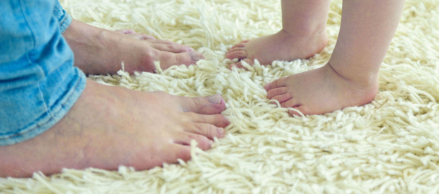 Füße von Mutter und Kind auf einem Teppich. 