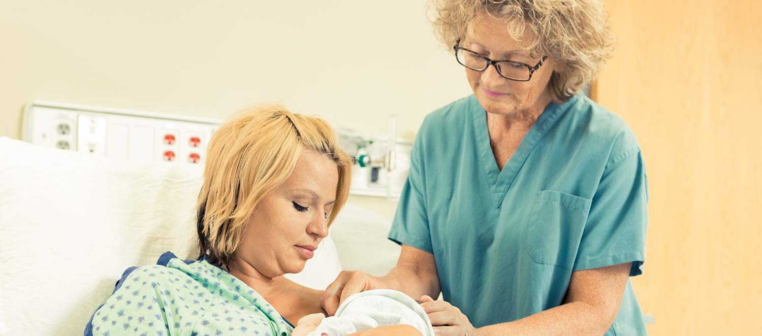 Im Krankenhaus-Zimmer: Hebamme steht bei Mutter und Baby am Bett. 