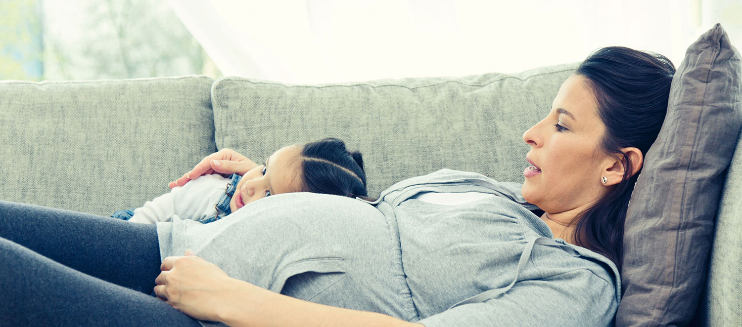 Schwangere Mutter liegt mit Tochter auf dem Sofa. 