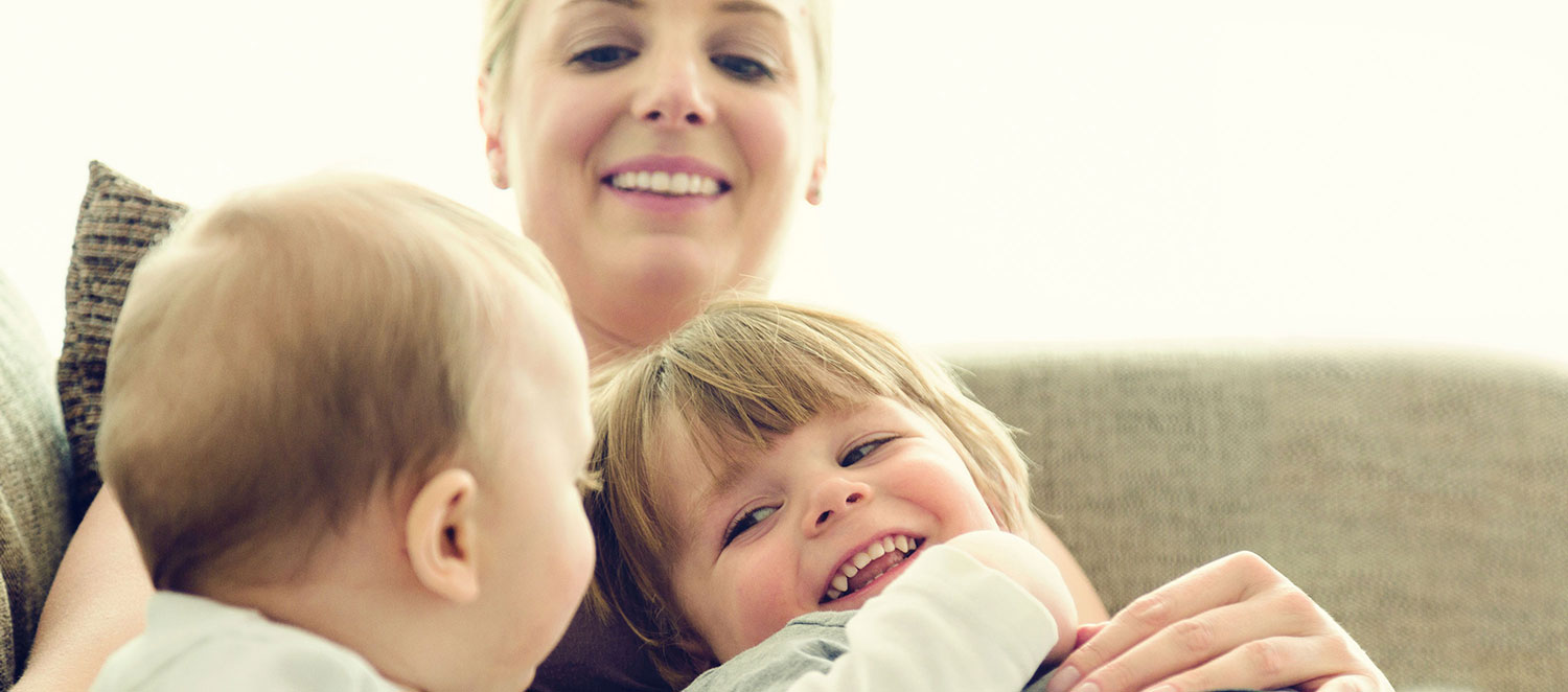 Mutter mit zwei Kleinkindern auf dem Sofa, lachend.