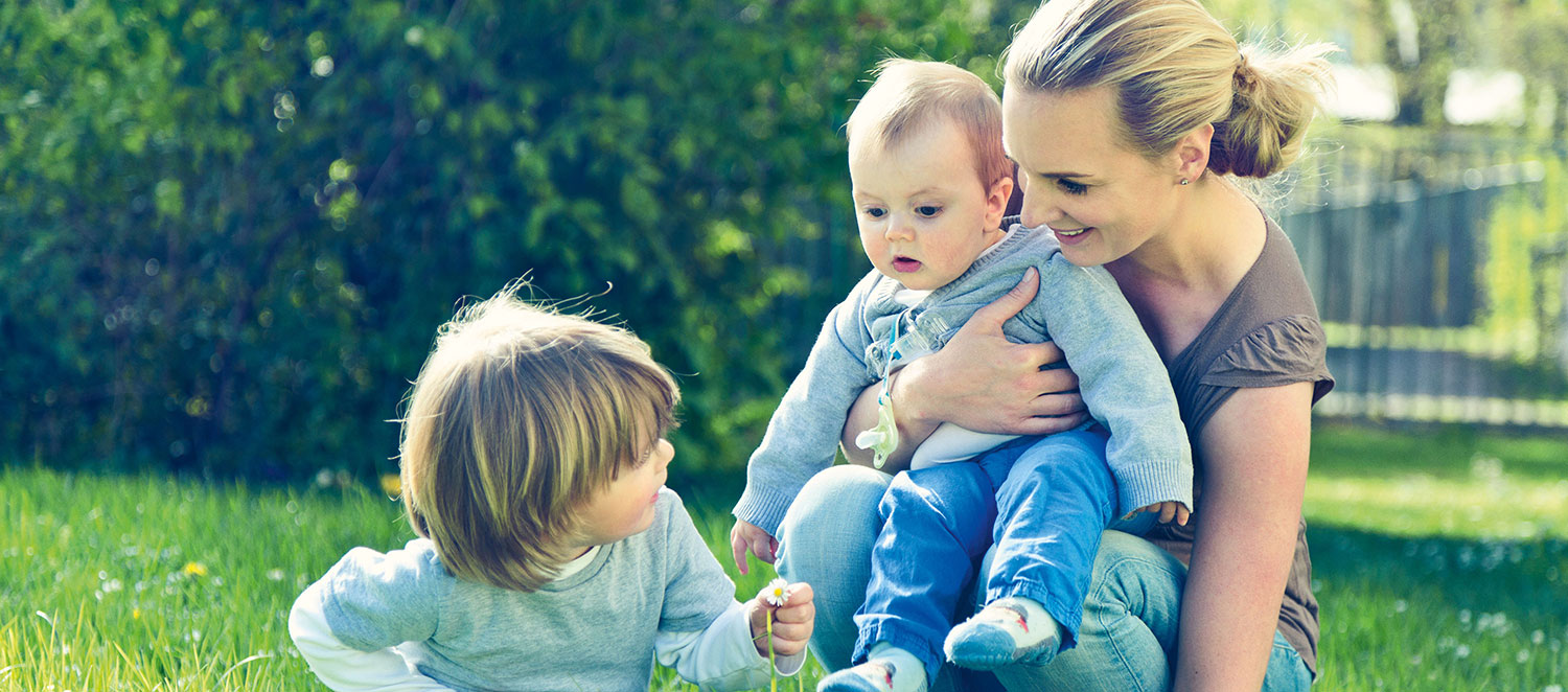 Frau mit zwei Kindern im Garten. 