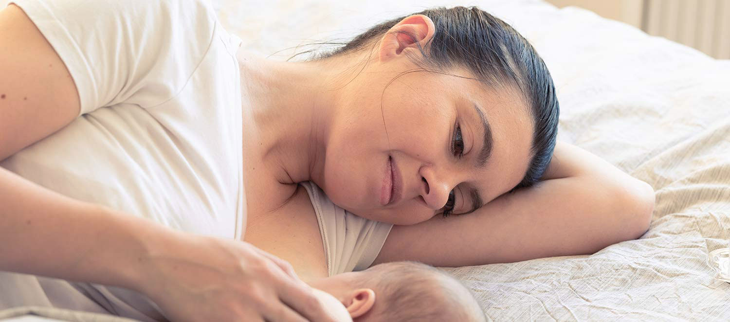 Mutter stillt Neugeborenes im Bett. 