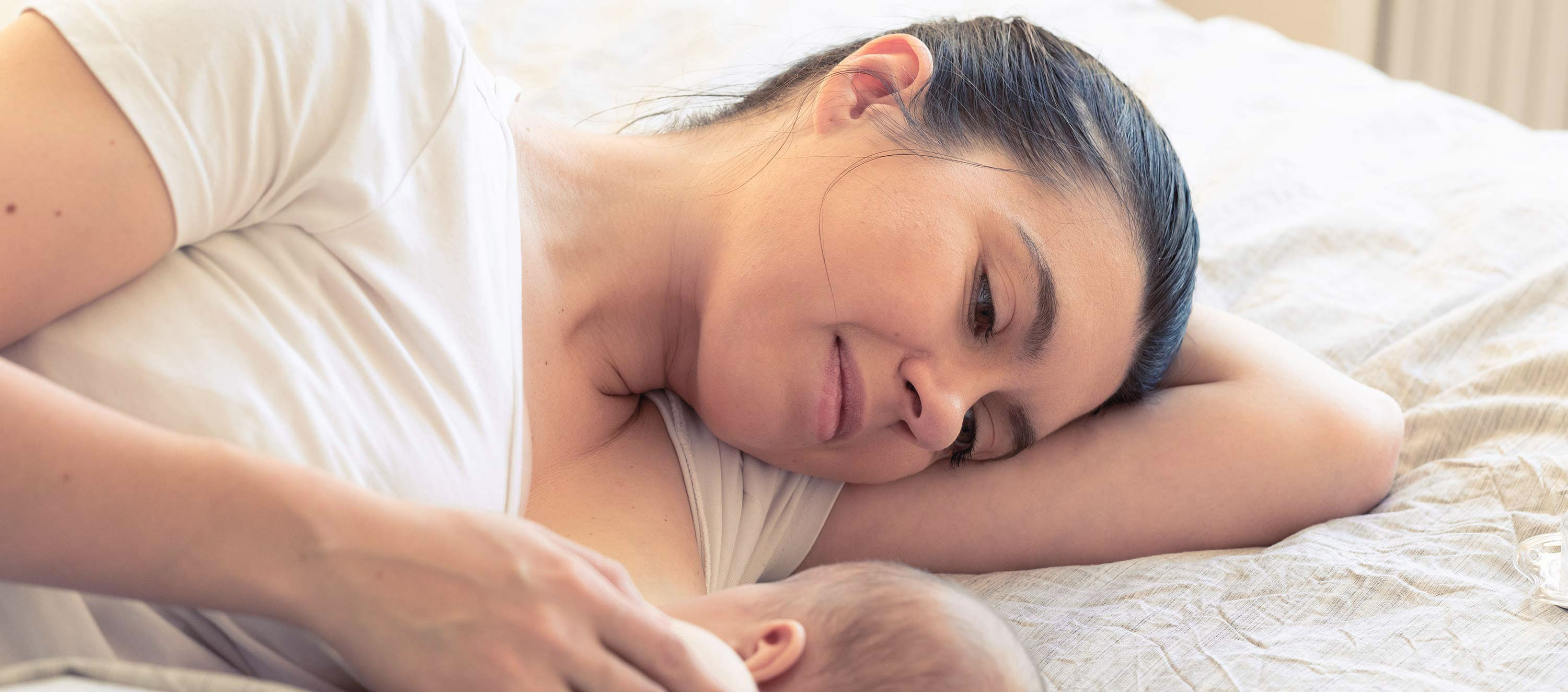 Frau liegt mit Säugling stillend im Bett liegen. 
