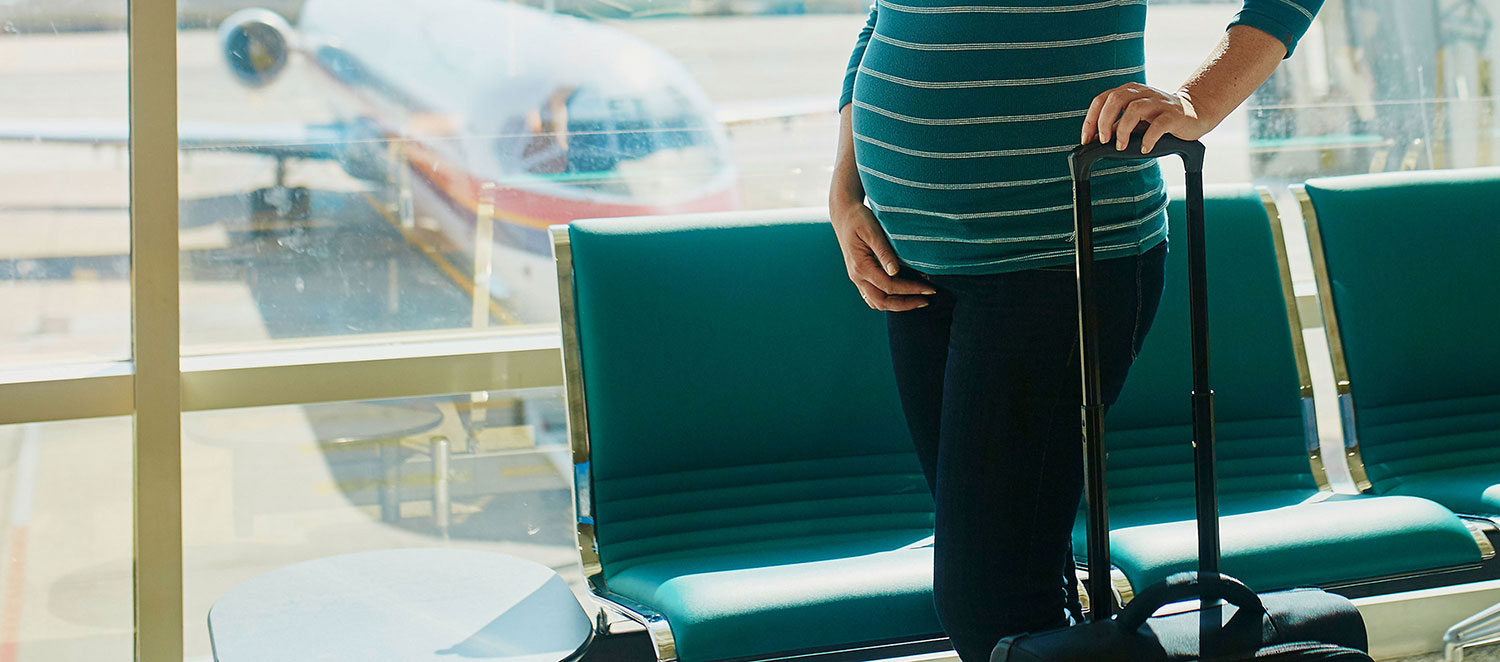Schwangere Frau mit Koffer am Flughafen. 