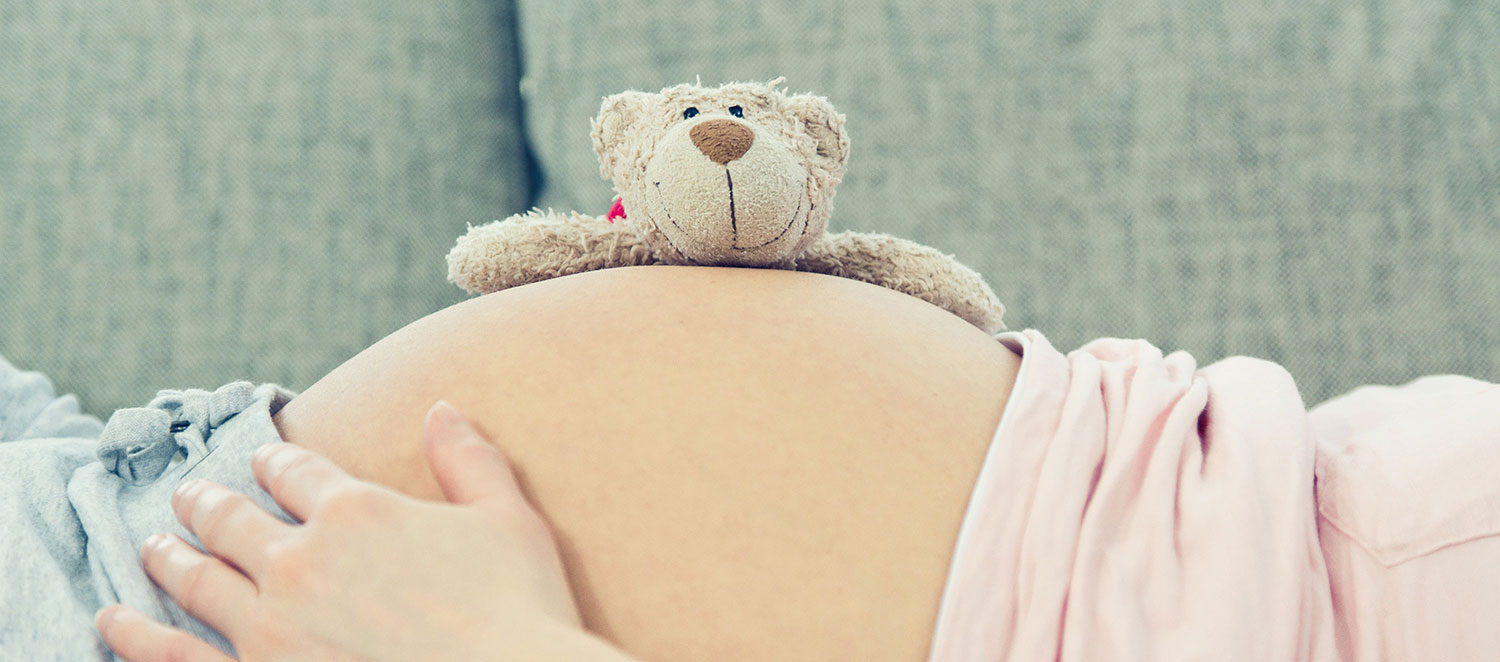 Schwangere liegend mit Teddybär auf Bauch