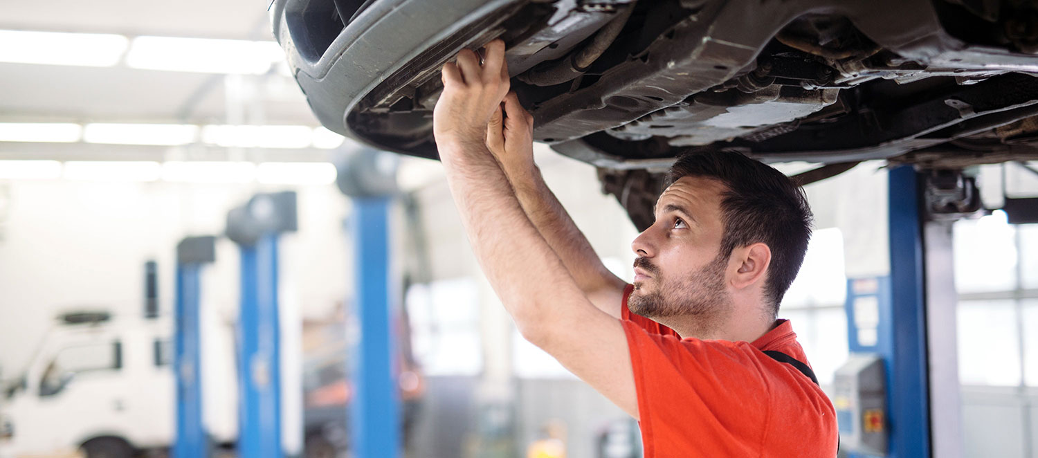 Mann arbeitet in einer KfZ-Werkstatt am Auto. 