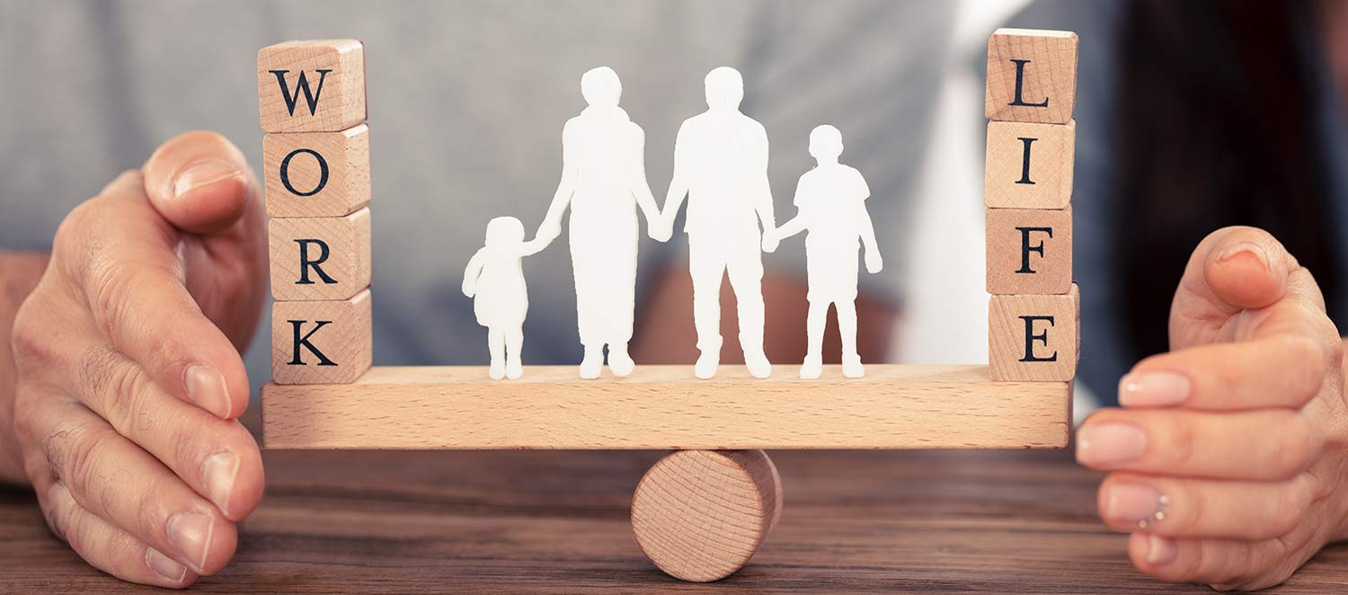 Paar beschützt mit den Händen symbolisch die Work-Life-Balance in Form von Figuren einer Familie auf einer Wippe. 