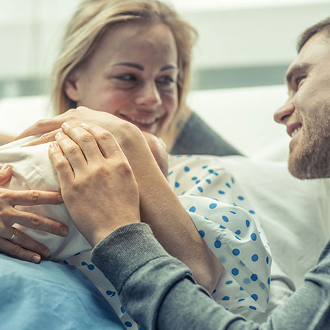 Im Krankenhaus-Zimmer: Mutter und Vater streicheln Neugeborenes. 