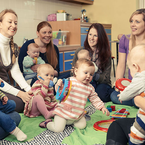 Eine Gruppe von Müttern mit spielenden Babys sitzt im Kreis. 