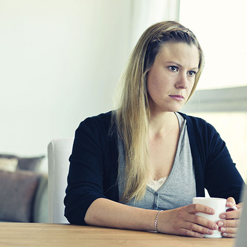 Nachdenkliche Frau mit Kaffeetasse sitzt am Tisch.