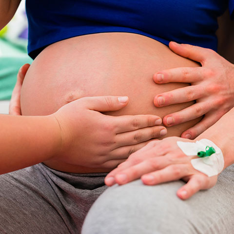 Hände tasten Bauch einer schwangeren Frau ab. 