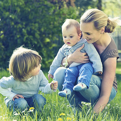 Frau mit zwei Kindern im Garten. 