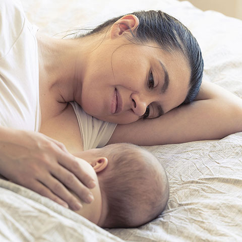 Nahaufnahme: Mutter stillt Neugeborenes im Bett. 