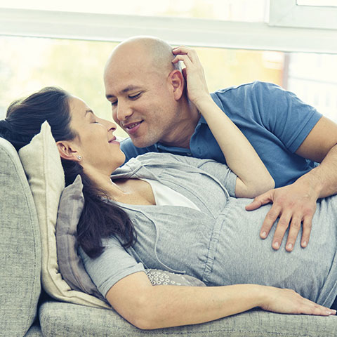 Mann und Frau liegen auf dem Sofa und schauen sich liebevoll an. 