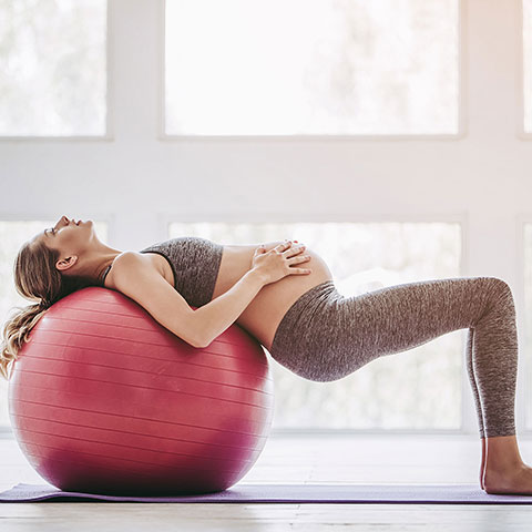 Schwangere Frau liegt auf Gymnastikball. 