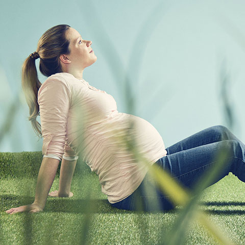 Hochschwangere Frau sitzt im Freien auf einer Wiese. 