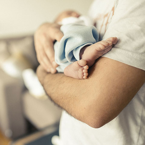 Zu Hause: Vater hält Neugeborenes im Arm. 