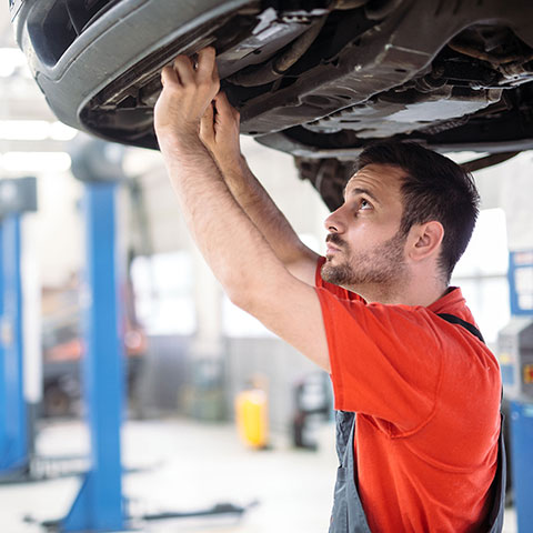 In der Auto-Werkstatt: Mann arbeitet unter einem Fahrzeug. 